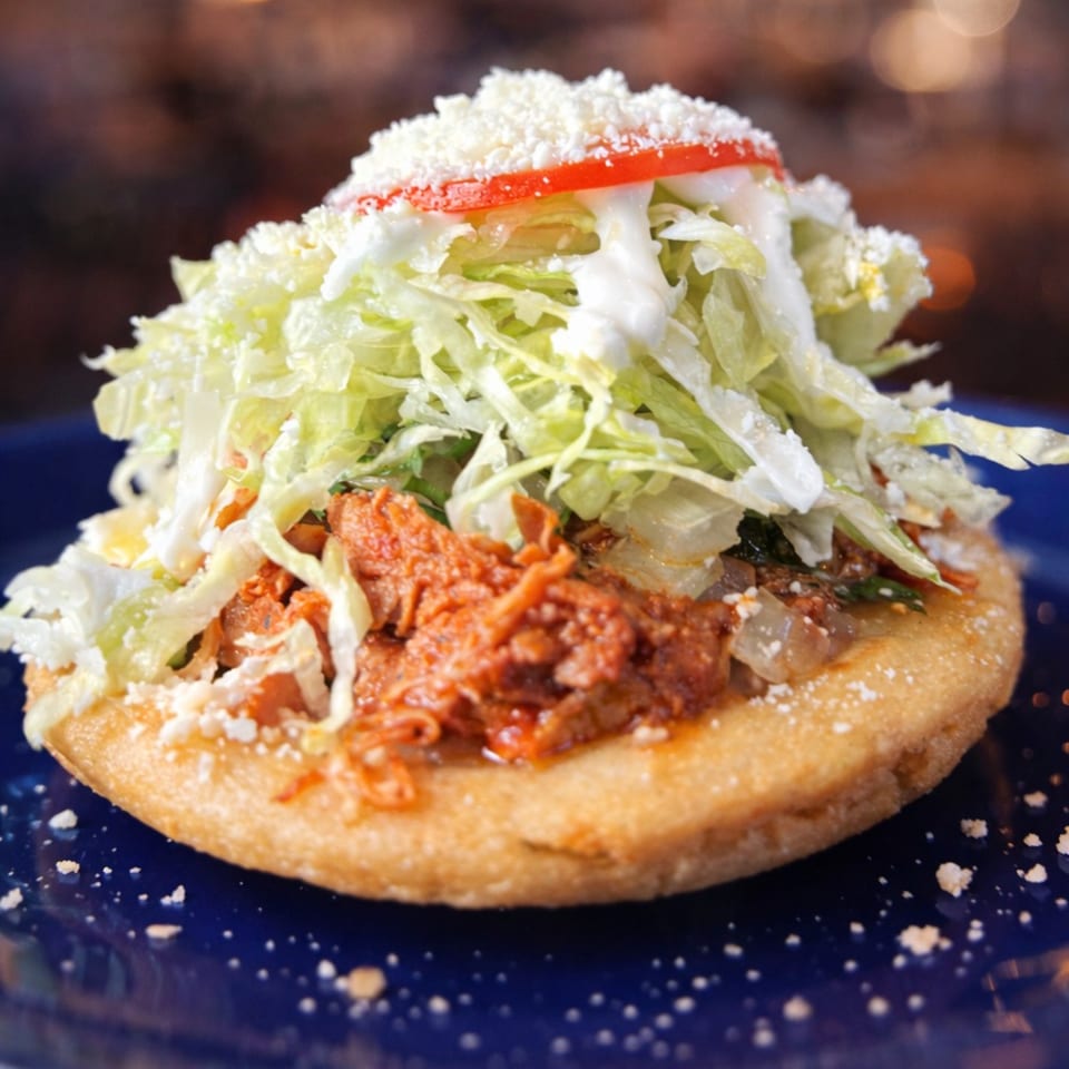 A Jalisco Taqueria sopes with shredded meat, lettuce, cheese, sour cream, and tomato.
