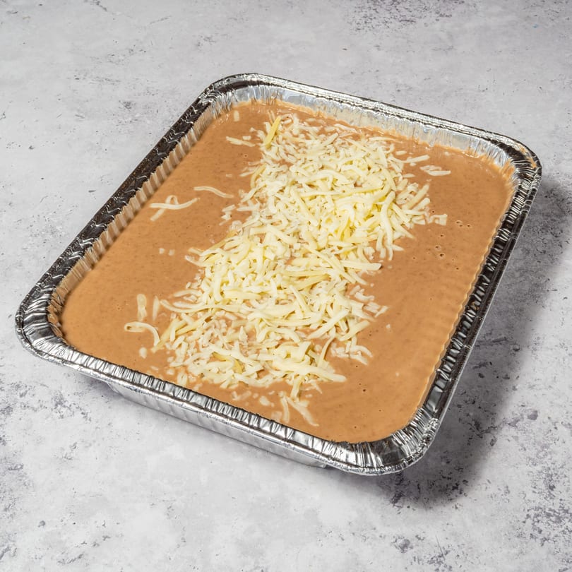 Refried beans topped with shredded cheese in a foil pan, ready for baking.