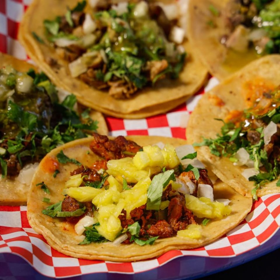 A close-up of several Jalisco Taqueria tacos with various toppings on a red and white checkered liner.